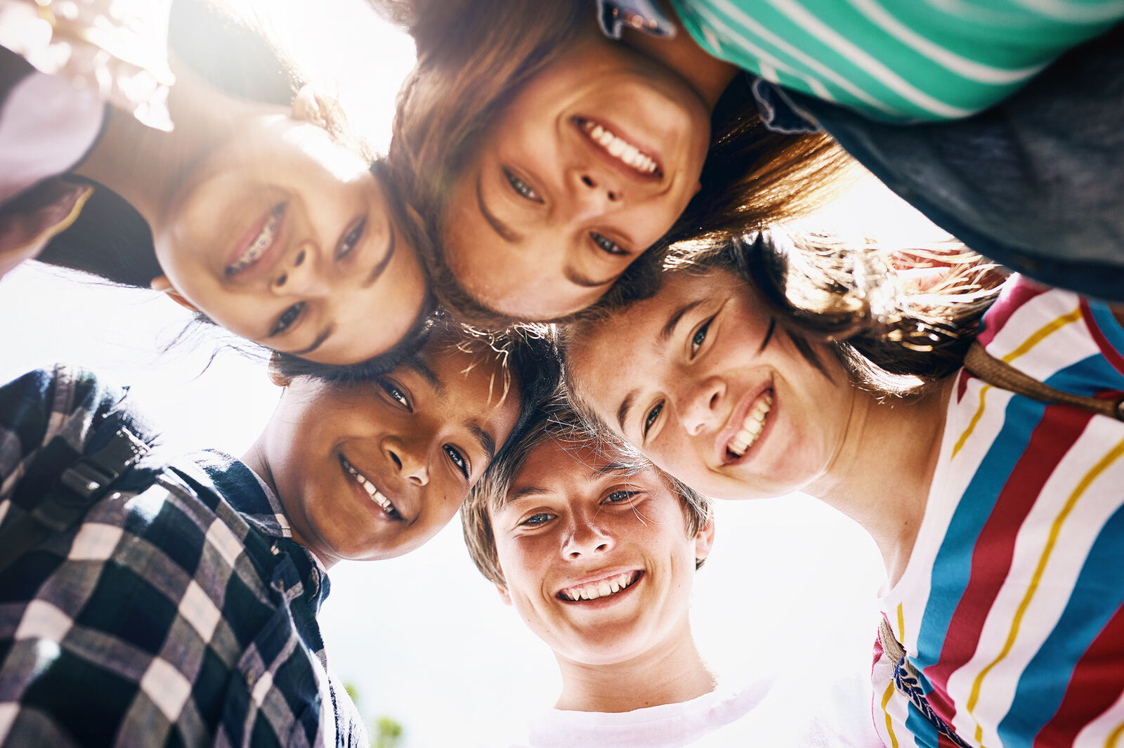 A group of middle-school-aged students huddled together outdoors, smiling up at the camera